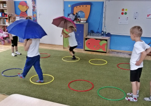 Dzieci pod parasolami wchodzą do kałuży- obręczy